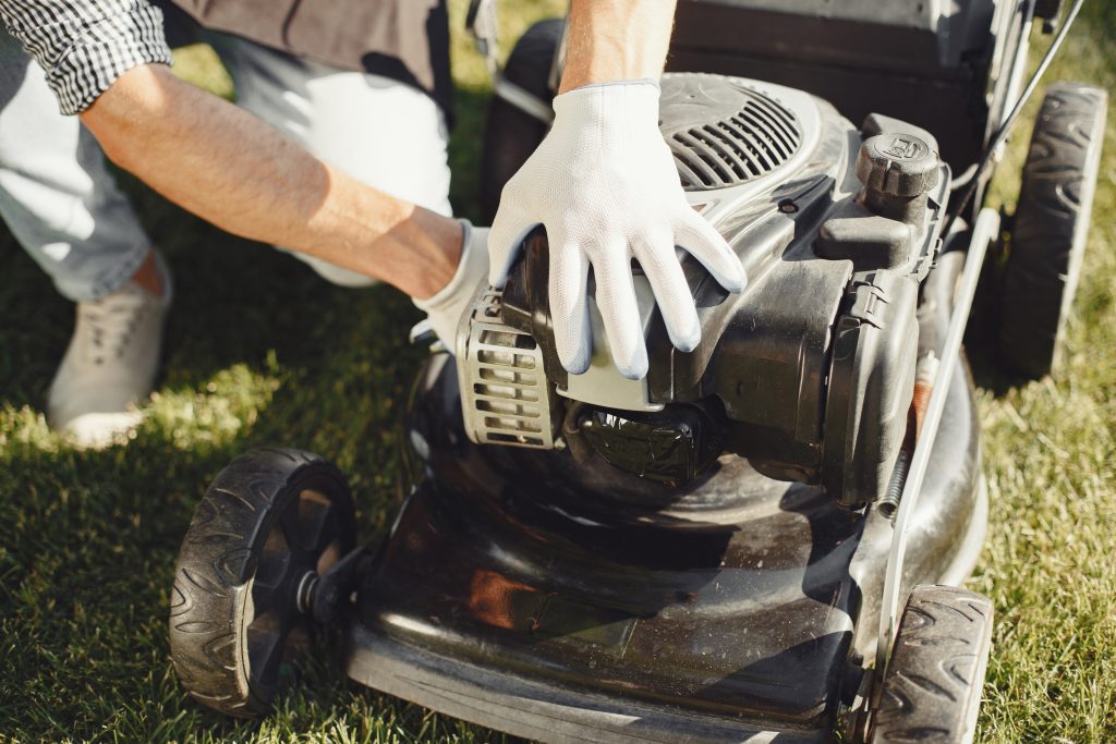 A male landscaper with white gloves leaning down to safely adjust a lawn mower's controls.
